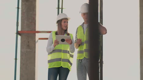 Building-in-construction-with-a-female-and-a-male-builders-constructors-engineers-walking-along-it.-Building-in-construction-with-a-female-and-a-male-engineers